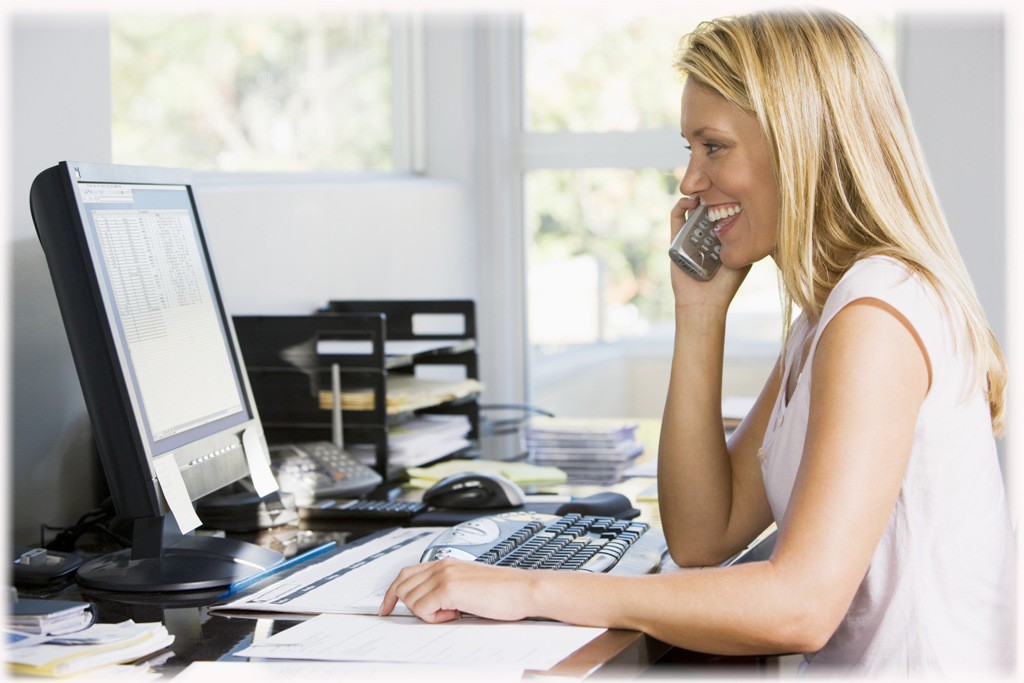 Woman In Home Office With Computer Using Telephone Smiling